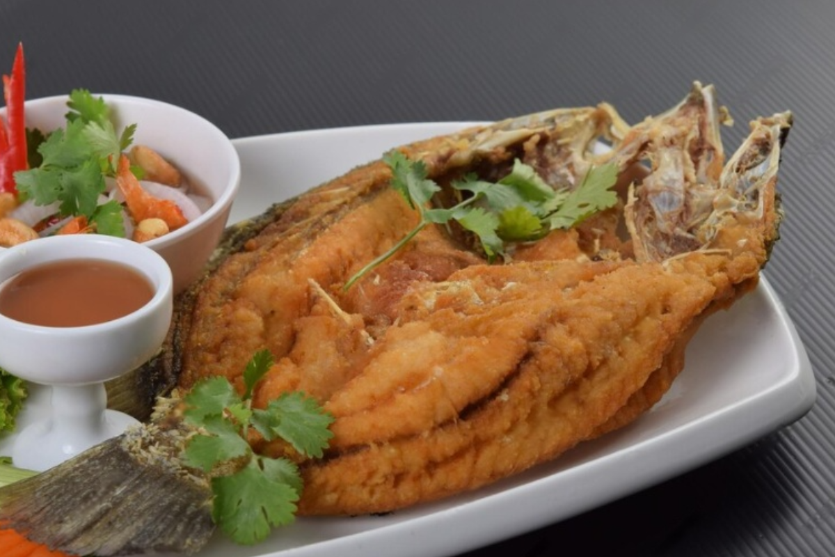 A crispy, golden-brown Fried Daing na Bangus on a plate, served with a side of vinegar dipping sauce. The marinated bangus belly is perfectly fried, with a crunchy texture and a deliciously flaky inside.